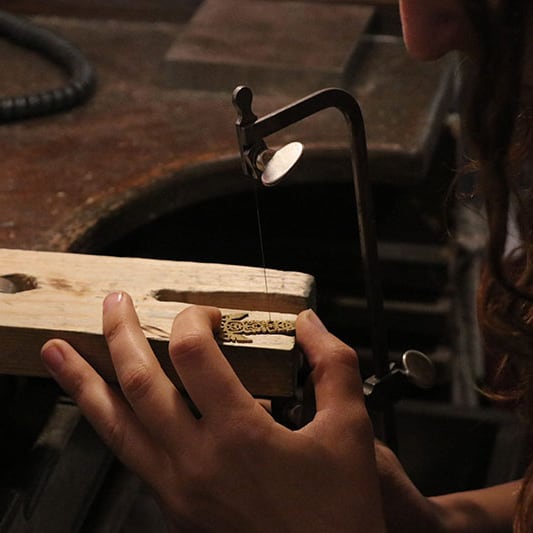 Hila hand-sawing a piece at her jeweler's bench